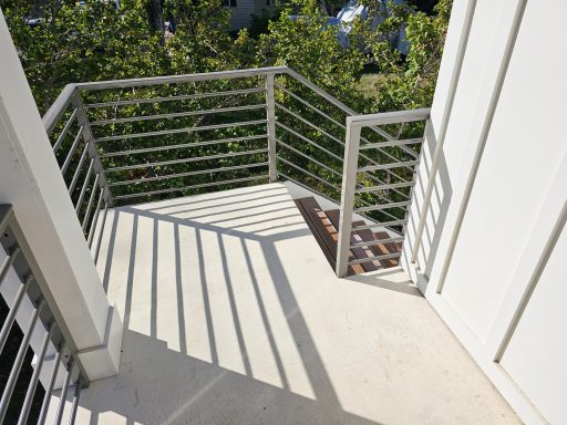 A corner balcony with modern railing and shadows cast on the concrete floor.